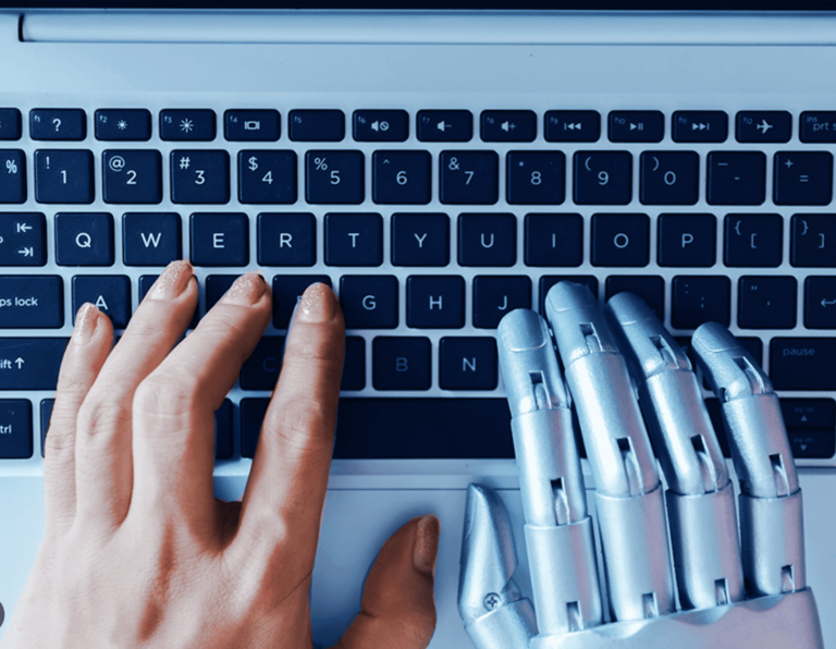 Close-up of a human hand and a robotic hand typing together on a laptop keyboard symbolizing human-AI collaboration