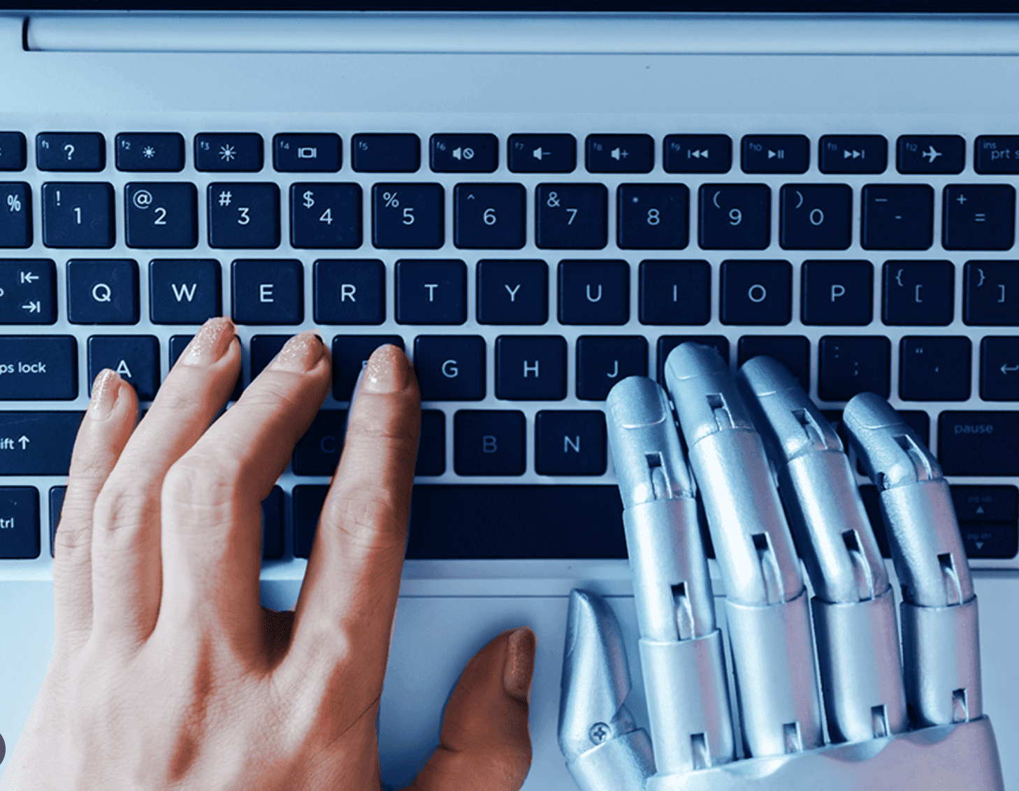 Close-up of a human hand and a robotic hand typing together on a laptop keyboard symbolizing human-AI collaboration